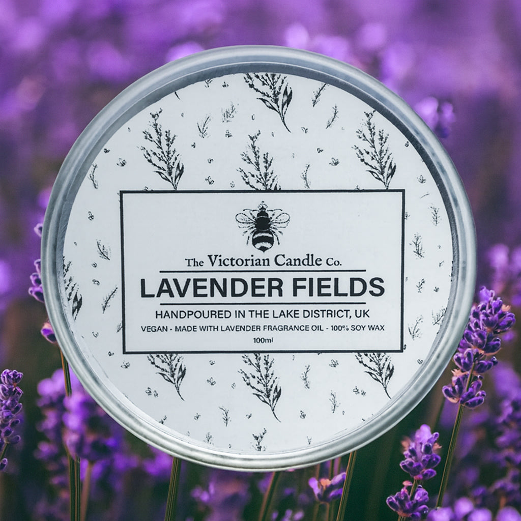 A round 100ml tin of The Victorian Candle Co’s Lavender Fields scented candle rests among fresh lavender, its label adorned with lavender art. This handmade UK candle offers relaxing aromatherapy.