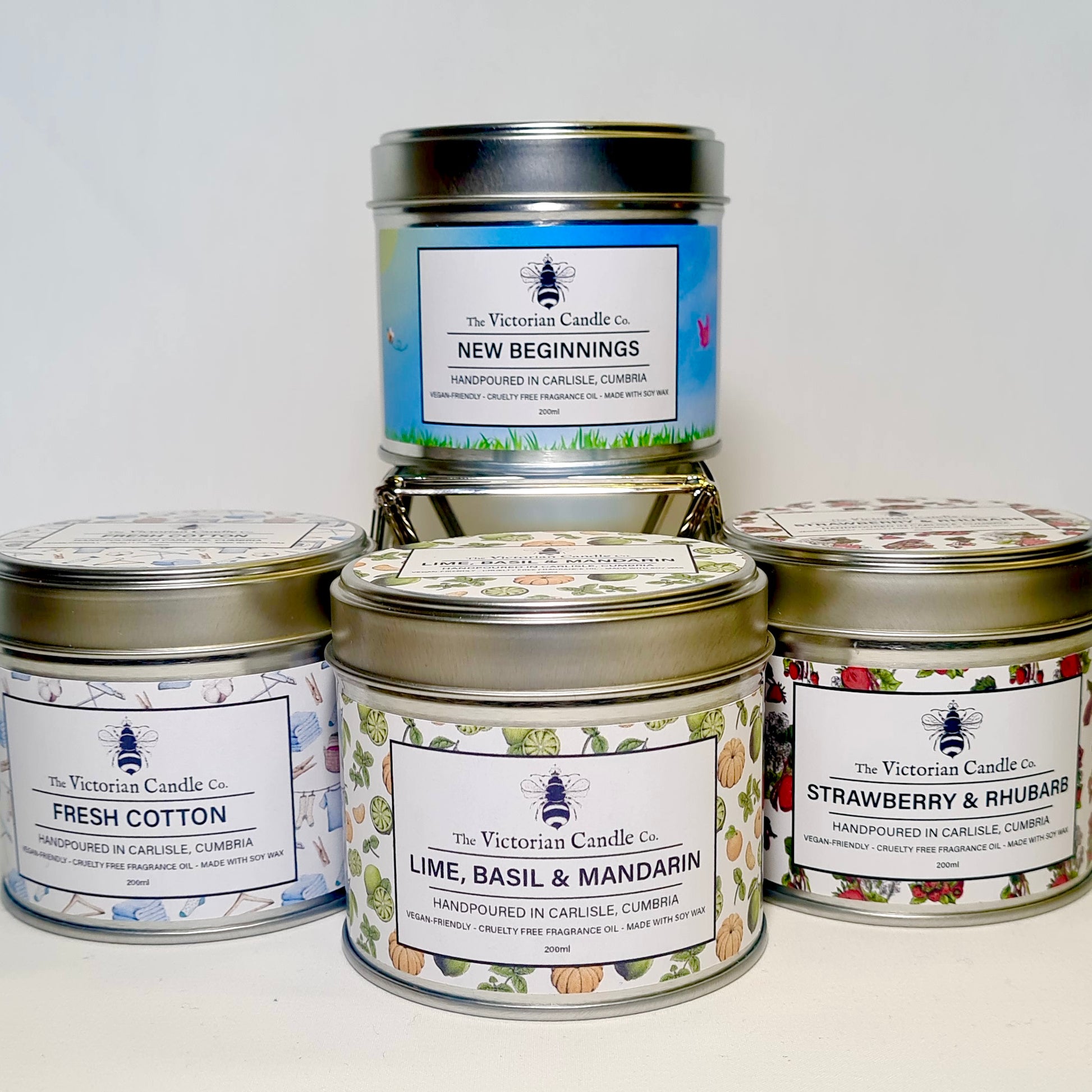 The Fresh Large Candle Collection Box from The Victorian Candle Co. showcases four decorative 200ml tins labeled New Beginnings, Fresh Cotton, Lime, Basil & Mandarin, and Strawberry & Rhubarb. Handcrafted in Carlisle, Cumbria, these candles are made with soy vegan-friendly wax and come in recyclable tins.