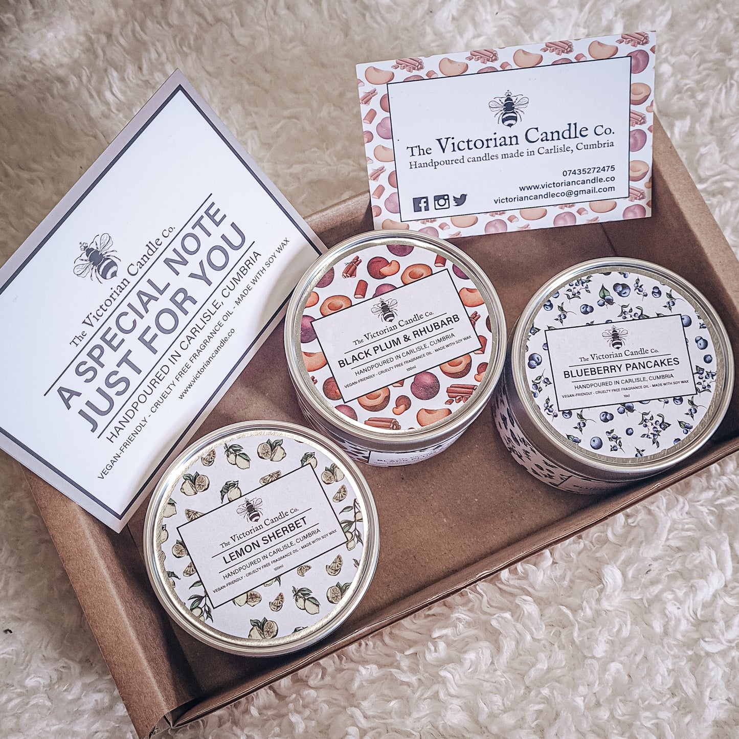 Introducing the Trio Small Candle Gift Box by The Victorian Candle Co.: a collection of three scented candles in tins named Lemon Sherbet, Black Plum & Rhubarb, and Blueberry Pancakes. Each candle is made with soy vegan-friendly wax. The set also includes a business card from The Victorian Candle Co. and a special note card.