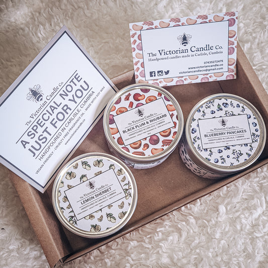 Introducing the Trio Small Candle Gift Box by The Victorian Candle Co.: a collection of three scented candles in tins named Lemon Sherbet, Black Plum & Rhubarb, and Blueberry Pancakes. Each candle is made with soy vegan-friendly wax. The set also includes a business card from The Victorian Candle Co. and a special note card.