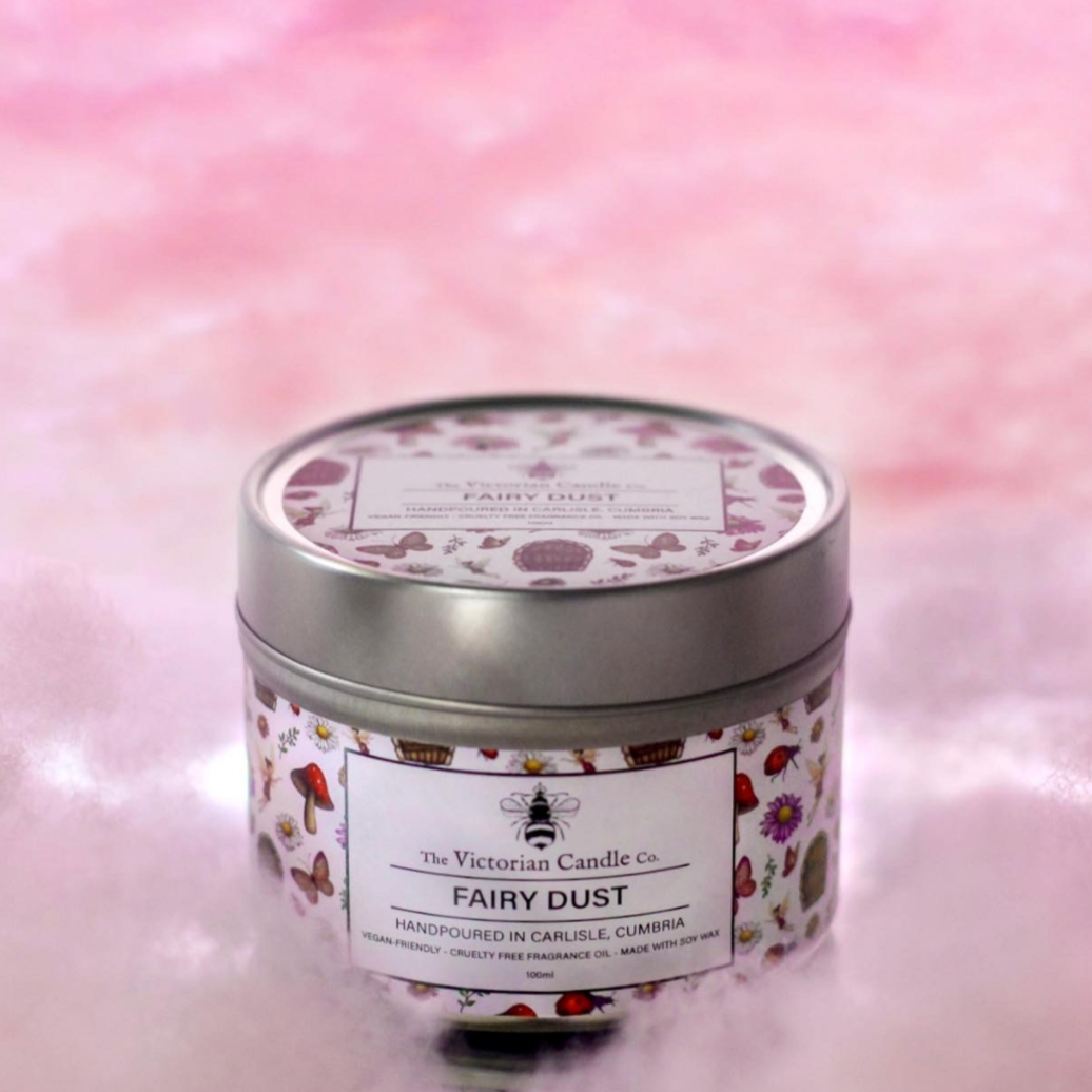A 100ml tin candle named "Fairy Dust" by The Victorian Candle Co. is crafted with soy vegan-friendly wax. It boasts charming illustrations of mushrooms and leaves, set against a delicate soft pink, cloud-like background, and it fills the air with captivating scents.