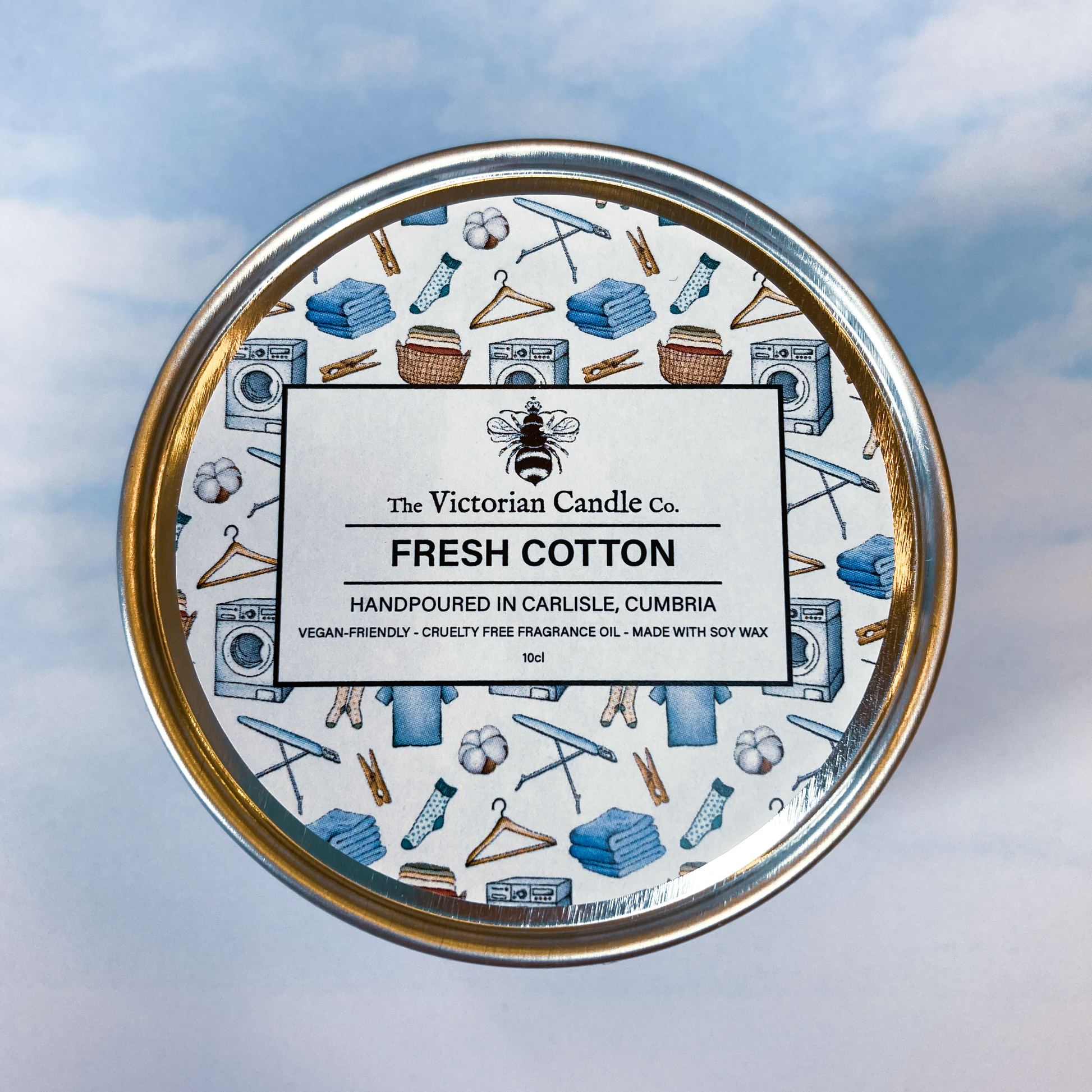 Top view of the 100ml Fresh Cotton Scented Candle tin by The Victorian Candle Co. The lid features illustrations of laundry items such as washers and hangers. Made in Carlisle, Cumbria, these candles are crafted with 100% soy vegan-friendly wax and come in recyclable tins.