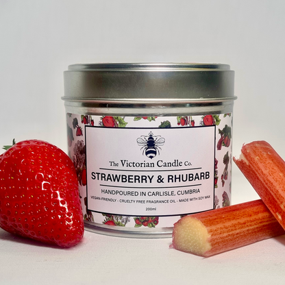 A large, 200ml soy wax scented candle by The Victorian Candle Co., called "Strawberry & Rhubarb," features floral accents and is accompanied by fresh strawberries and rhubarb stalks. The label emphasizes its vegan and cruelty-free qualities.