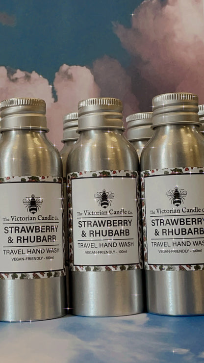 A collection of 100ml silver bottles from The Victorian Candle Co., featuring their vegan-friendly Strawberry & Rhubarb Travel Hand Wash, is arranged against a backdrop of clouds.