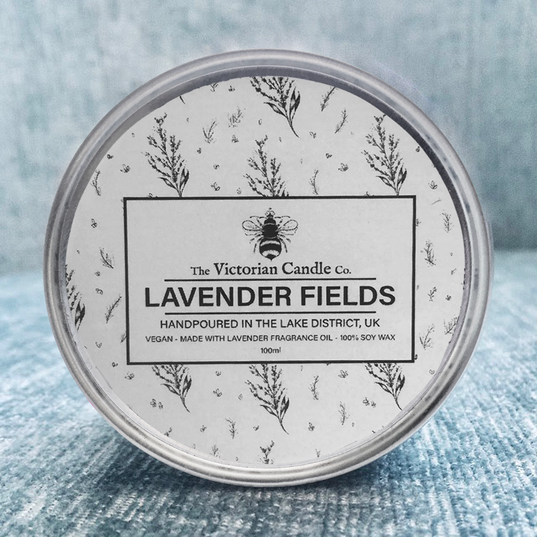 A 100ml tin of the Victorian Candle Co's Lavender Fields scented candle rests on a textured blue surface. This hand-poured, vegan-friendly candle from the Lake District is made with 100% soy wax and infused with a calming lavender fragrance oil.