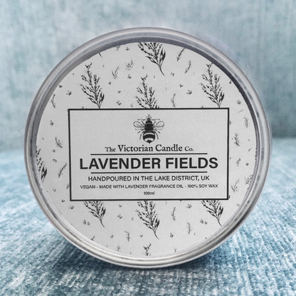 A 100ml tin of the Victorian Candle Co's Lavender Fields scented candle rests on a textured blue surface. This hand-poured, vegan-friendly candle from the Lake District is made with 100% soy wax and infused with a calming lavender fragrance oil.