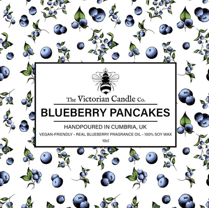 A patterned design of blueberries and leaves encircles a label that says: The Victorian Candle Co. Blueberry Pancakes - Scented Candle - 100ml Tin, Handpoured in Cumbria, UK. This vegan-friendly candle is crafted with 100% soy wax and infused with real blueberry fragrance oil to offer a fruity home fragrance.