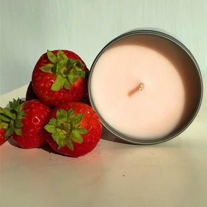 A light pink 100ml tin of the Strawberry & Rhubarb Scented Candle from The Victorian Candle Co. rests on a white surface, surrounded by fresh strawberries. Soft lighting accentuates the candle’s smooth, soy vegan-friendly wax and the strawberries' vibrant red color.